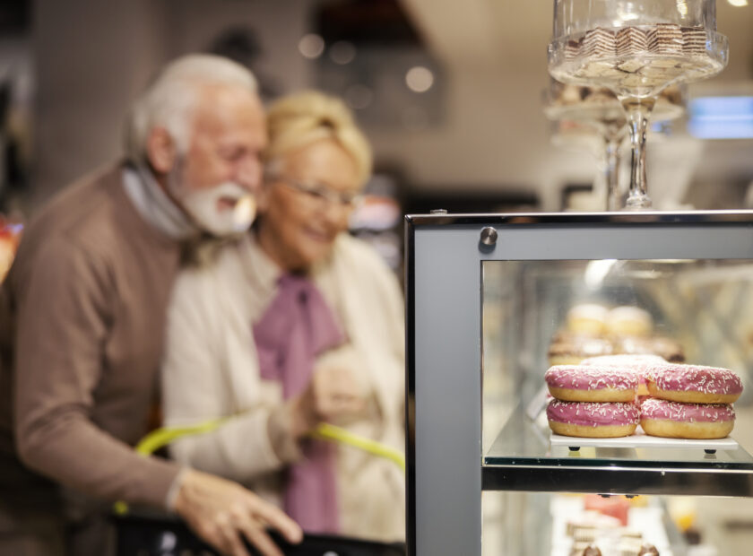 Selective focus on a delicious doughnuts at supermarket while senior couple choosing pasty in blurry background.